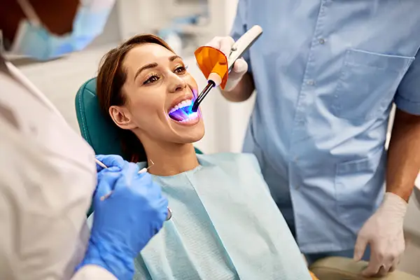 Dentist and assistant performing a dental bonding procedure on a female patient