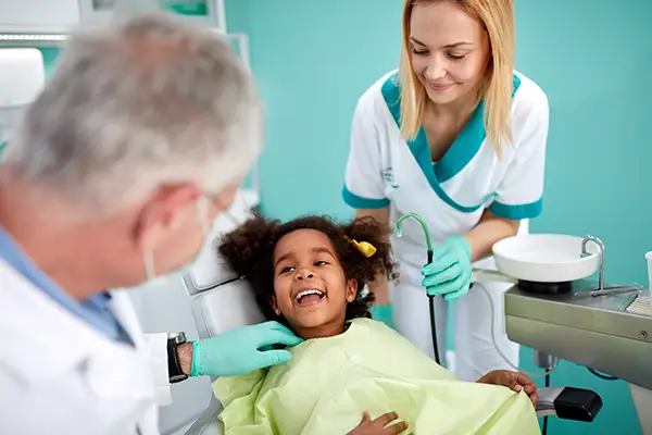Adorable and young Black girl sitting in a dental chair and smiling at her older white dentist and white dental assistant